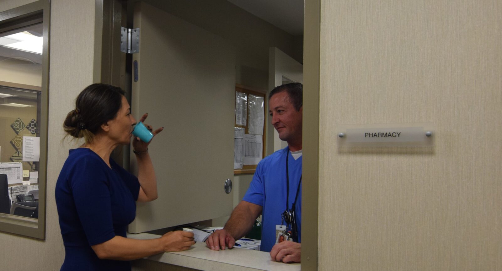 A nurse at the pharmacy window handing a client a cup
